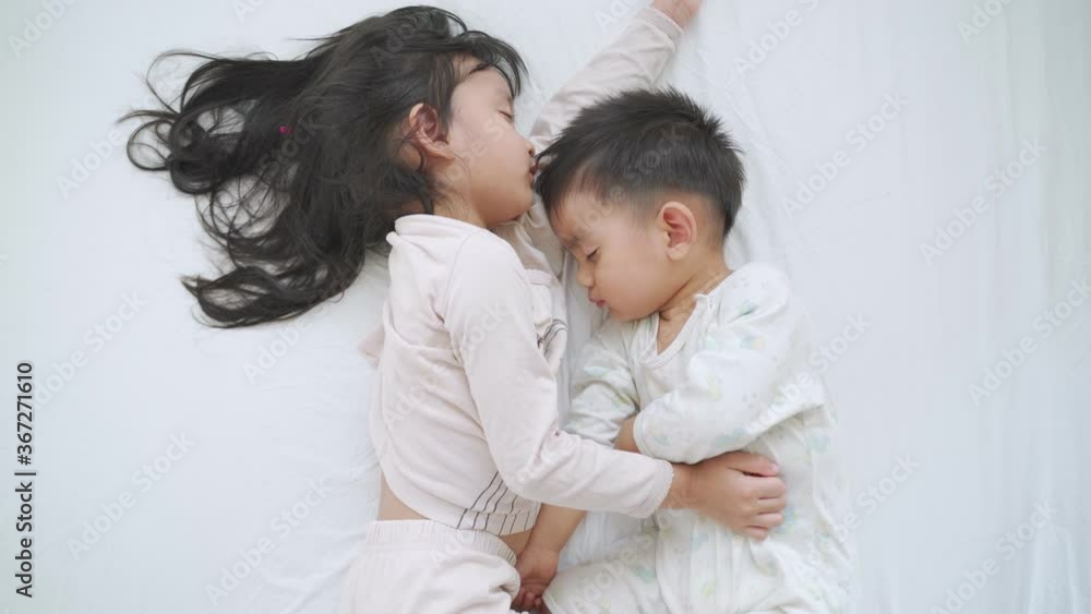 Asian sibling of sister and brother are sleeping together on the white bed in the morning time. Asian sibling of sister and brother are sleeping together on the white bed in the morning time.