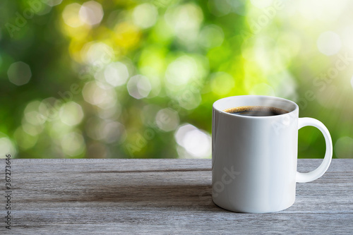 Hot white coffee cup on wooden tabletop on blurred green nature bokeh background