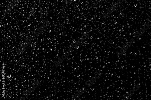 Drops of water flow down the surface of the clear glass on a black background. Texture for creativity.