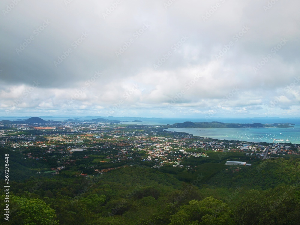 Panoramic view from the top to the bottom to the tropical coastal town. Sea harbour. Turquoise water and sky with gray cumulus clouds. Seascape. Islands, green forest, rainforest, jungle