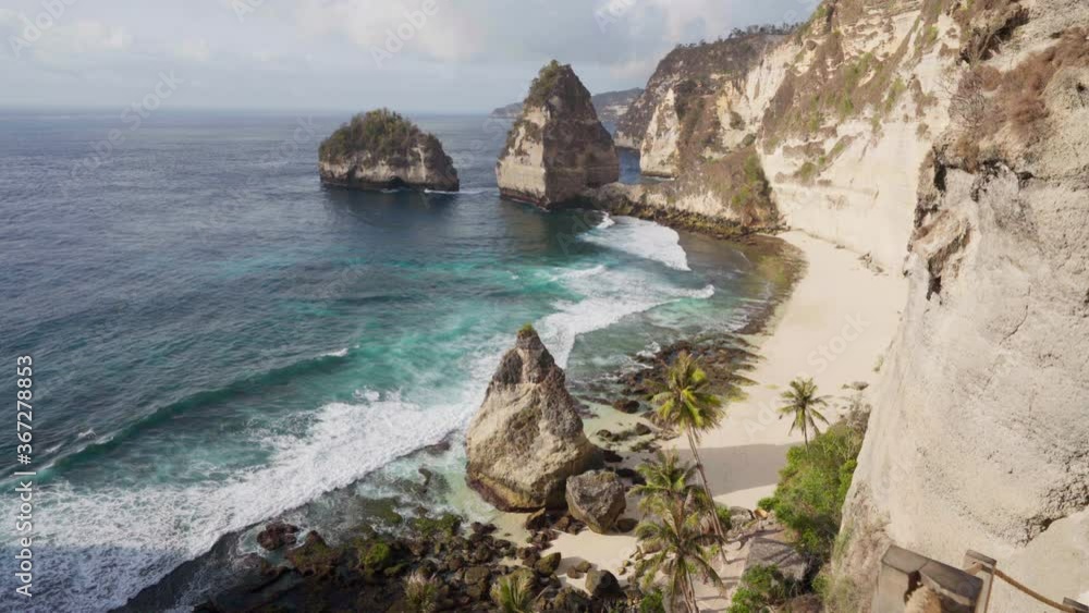 Top view on coastline Diamond Beach with a crystal clear sea lagoon and sandy beach with beautiful palm tree on background of scenery nature landscape. Nusa Penida, Indonesia 4K Top view on coastline Diamond Beach with a crystal clear sea lagoon and sandy beach with beautiful palm tree on background of scenery nature landscape. Nusa Penida, Indonesia 4K