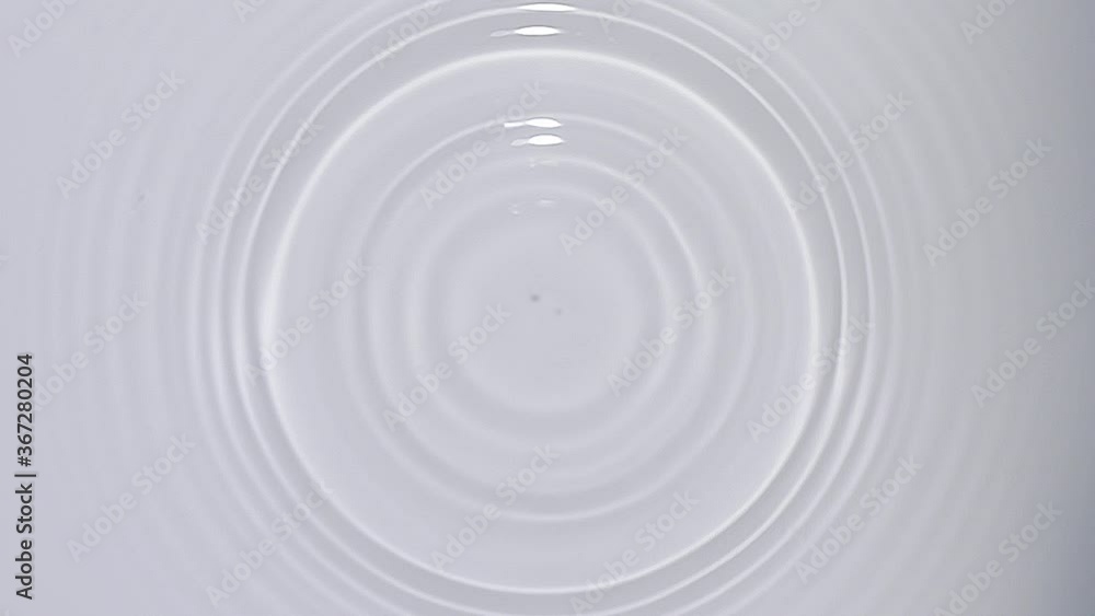 Top view of drop falls into water and diverging circles of water on white background in slow motion