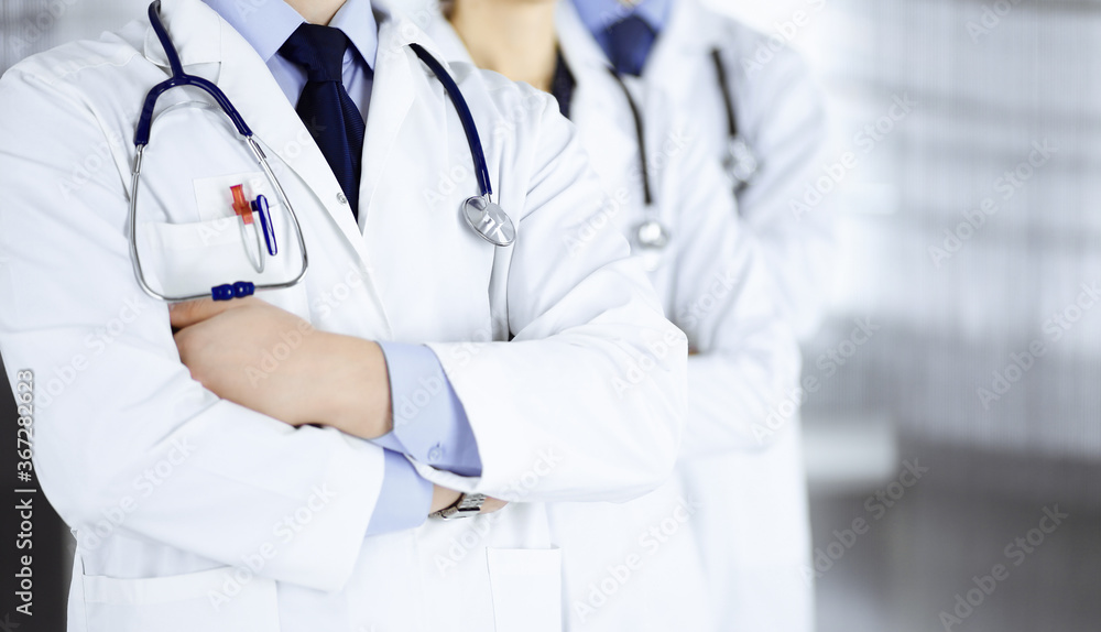 Group of modern doctors standing as a team with crossed arms and stethoscopes in hospital office. Physicians ready to examine and help patients. Medical help, insurance in health care, best desease Group of modern doctors standing as a team with crossed arms and stethoscopes in hospital office. Physicians ready to examine and help patients. Medical help, insurance in health care, best desease