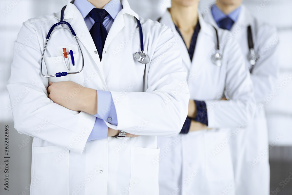 Group of modern doctors standing as a team with crossed arms and stethoscopes in hospital office. Physicians ready to examine and help patients. Medical help, insurance in health care, best desease Group of modern doctors standing as a team with crossed arms and stethoscopes in hospital office. Physicians ready to examine and help patients. Medical help, insurance in health care, best desease