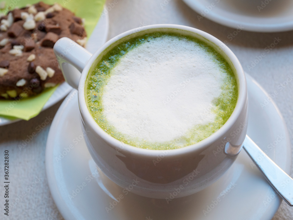 A cup of matcha latte and a chocolate chip cookie. A hot drink of green color. Breakfast concept. A cup of matcha latte and a chocolate chip cookie. A hot drink of green color. Breakfast concept.