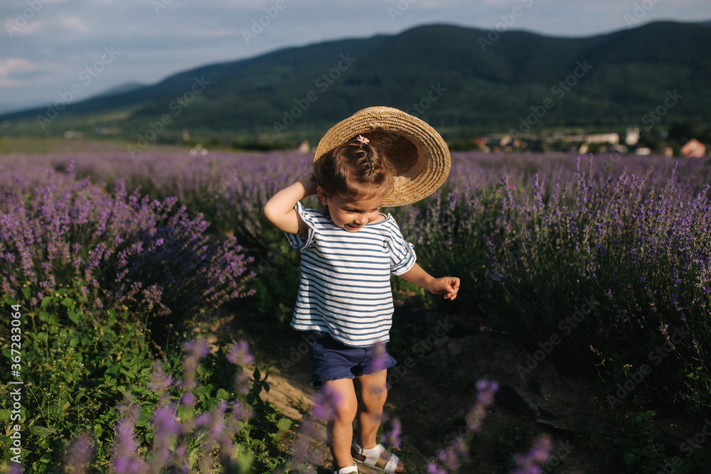 Happy little girl in straw hat walking in summer lavender field