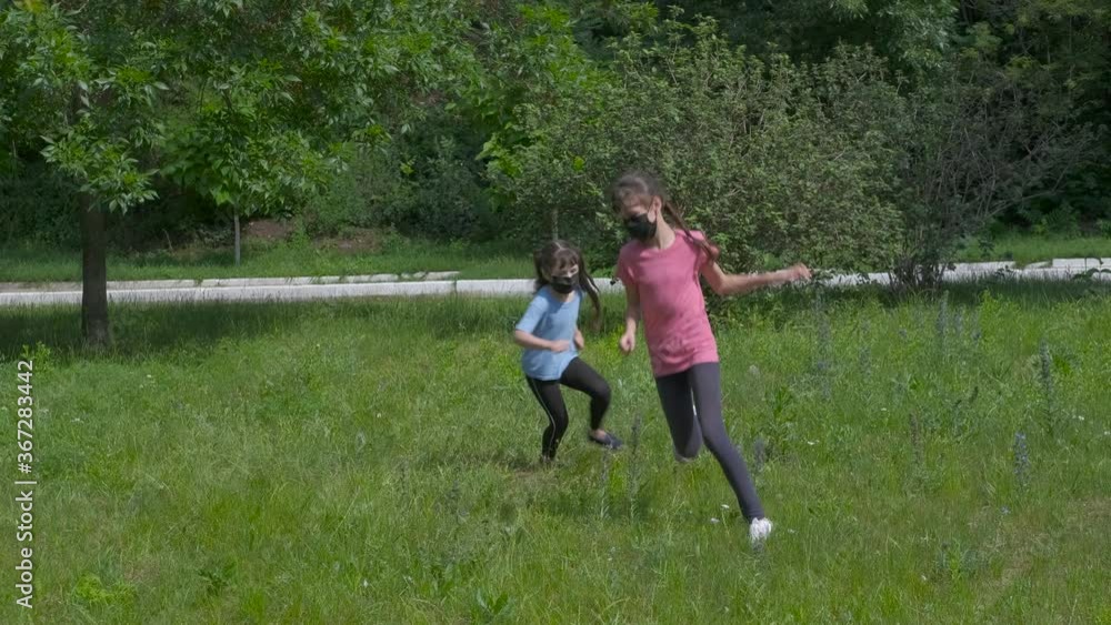 Leisure in epidemic time. Little girls in medical masks play on the summer lawn. Childhood in protective masks.