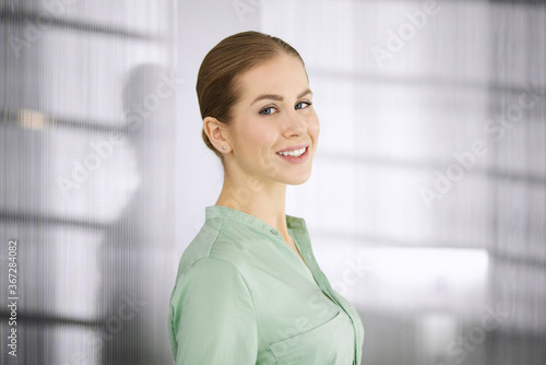 Beautiful adult business woman dressed in green blouse standing straight in office. Business headshot or portrait