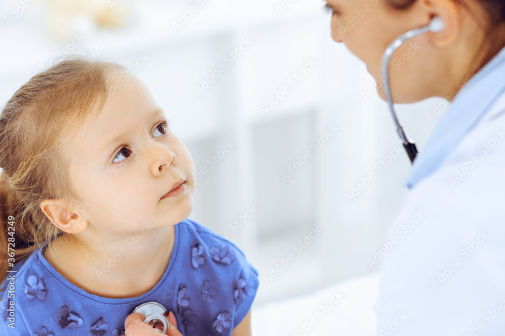 Doctor examining a little girl by stethoscope. Happy smiling child patient at usual medical inspection. Medicine and healthcare concepts Doctor examining a little girl by stethoscope. Happy smiling child patient at usual medical inspection. Medicine and healthcare concepts