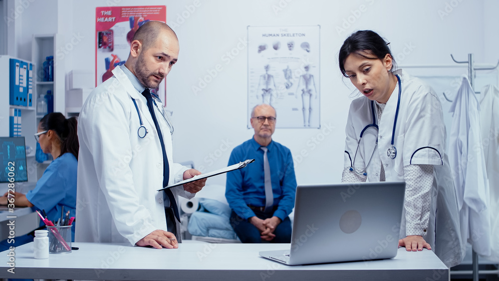 Team of man and woman doctors discussing elderly patient problem while he is in hospital bed worrying. Healthcare in modern hospital or private clinic, disease prevention and consultation in medic Team of man and woman doctors discussing elderly patient problem while he is in hospital bed worrying. Healthcare in modern hospital or private clinic, disease prevention and consultation in medic