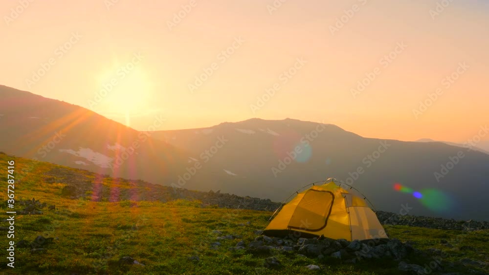 A tourist tent stands against the backdrop of a beautiful mountain landscape in the rays of the setting sun. Camp of tourists on the pass. Hiking in the mountains of the Northern Urals, Russia. A tourist tent stands against the backdrop of a beautiful mountain landscape in the rays of the setting sun. Camp of tourists on the pass. Hiking in the mountains of the Northern Urals, Russia.
