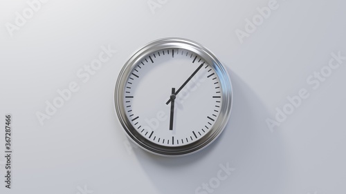 Glossy chrome clock on a white wall at seven past six. Time is 06:07 or 18:07