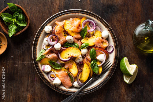 Refreshing summer salad with smoked salmon, peaches, mozzarella, red onion and basil. Wooden background.