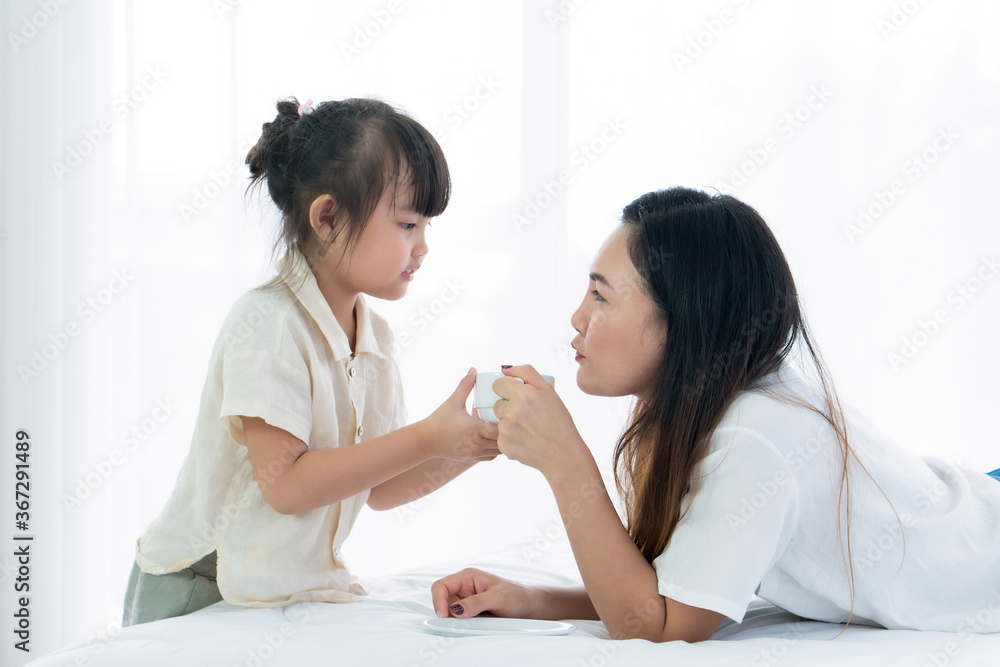 young asian handling tea cup to her asian mother who lying on the bed in bedroom at home. family together and relationship concept young asian handling tea cup to her asian mother who lying on the bed in bedroom at home. family together and relationship concept