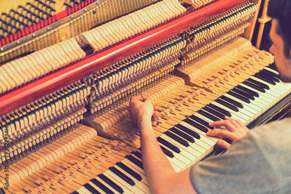 Piano tuning process. closeup of hand and tools of tuner working on grand piano. Detailed view of Upright Piano during a tuning Piano tuning process. closeup of hand and tools of tuner working on grand piano. Detailed view of Upright Piano during a tuning