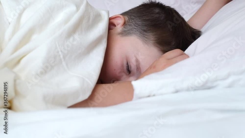 little child boy falling asleep in white bed lying on soft pillow. caucasian young baby kid sleeping deep covered with white blanket in morning bedroom. head of dreamy kid fall down into bed.