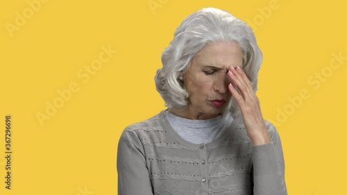 Overhelmed senior woman on color background. Unhappy mature woman looking pensive standing against yellow background. photo