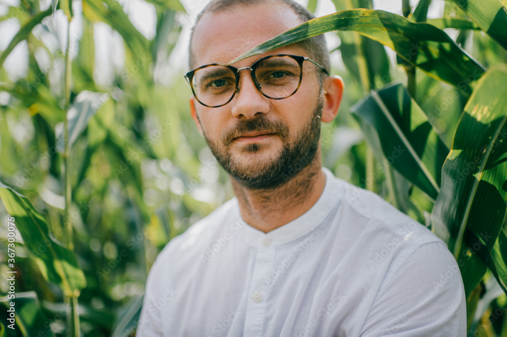 Attractive lonely caucasian man with short dadrk hair, black bristles on his face with glasses and a white shirt walks in cornfield Attractive lonely caucasian man with short dadrk hair, black bristles on his face with glasses and a white shirt walks in cornfield