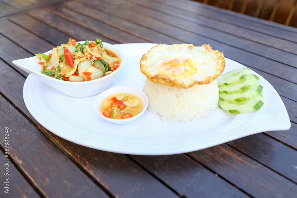 Pad Ka-prao; stir fried chopped chicken with chili and basil, served with steamed rice and fried egg on top set on wooden table Pad Ka-prao; stir fried chopped chicken with chili and basil, served with steamed rice and fried egg on top set on wooden table