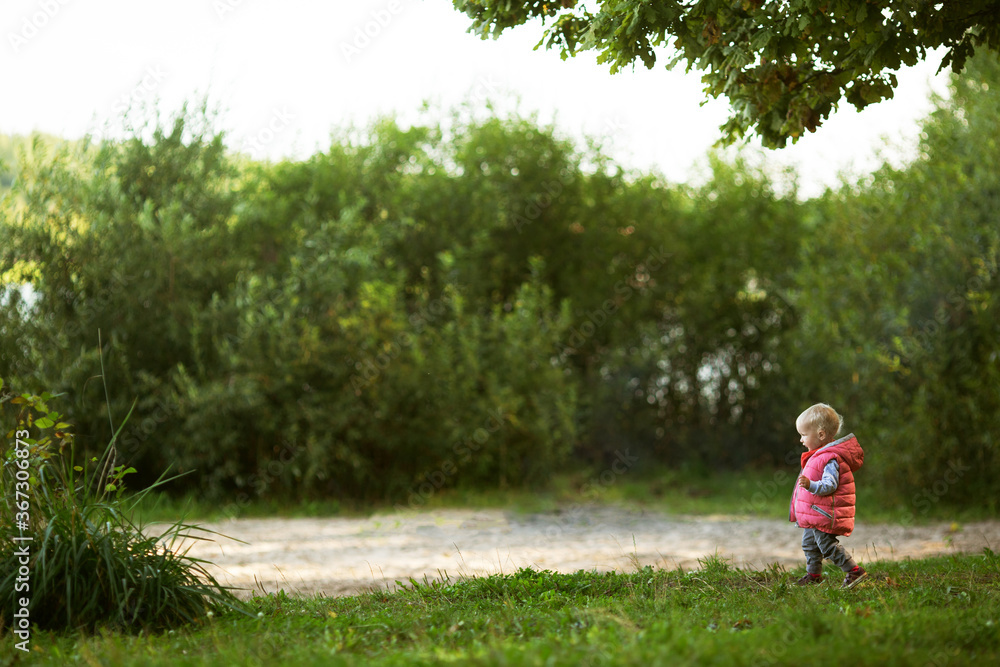 Baby girl with blond hair wearing pink waistcoat walking in green park exploring the big and interesting world Baby girl with blond hair wearing pink waistcoat walking in green park exploring the big and interesting world