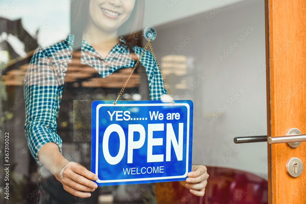 Closeup hand of Asian young woman setting open sign at the shop glasses for welcome the customer in to the coffee shop, small business owner and startup, installing open and close label concept
