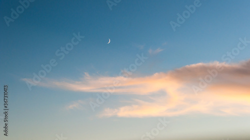 evening sky with moon and clouds. Golden warm pastel clouds. sunset giving Golden colors to the sky. blue sky with a white moon in the sky.