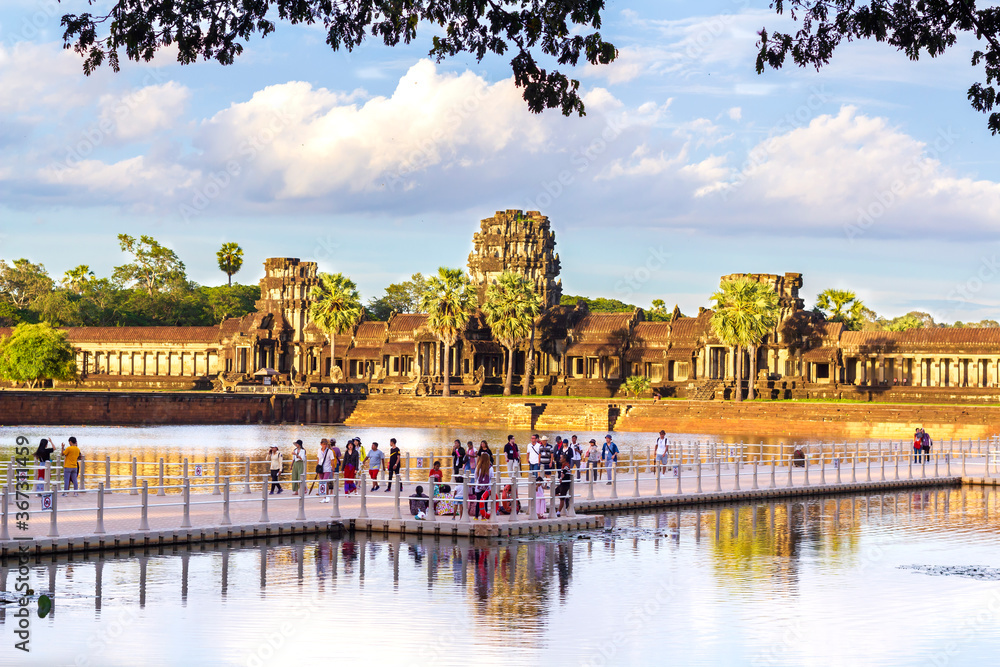 Naklejka premium turyści tłoczący się na kładce nad wodą przed świątynią Angkor wat, aby oglądać zachód słońca.