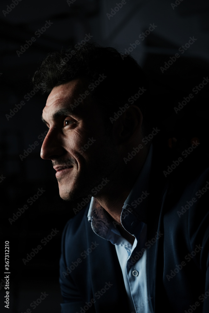 Fototapeta premium Close up portrait of a serious man 30-34 years old in a blue shirt and a dark jacket on a black background.