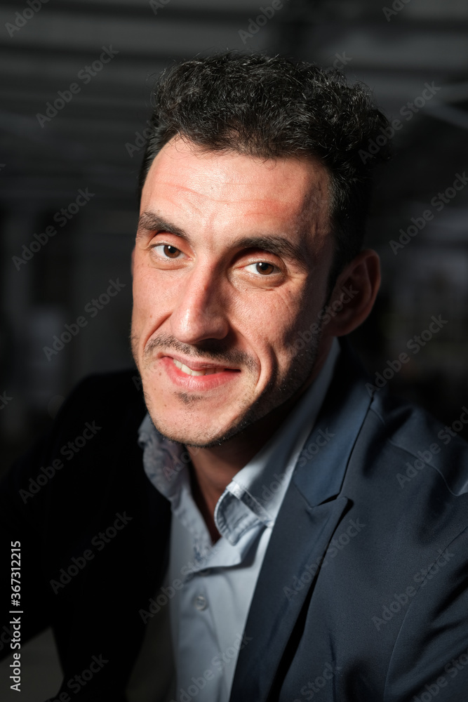 Close up portrait of a serious man 30-34 years old in a blue shirt and a dark jacket on a black background.