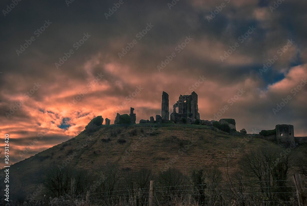 The sun rises behind the ruins of Corfe Castle in Dorset, UK
