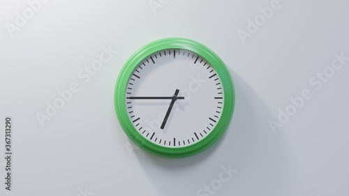 Glossy green clock on a white wall at quarter to seven. Time is 06:45 or 18:45