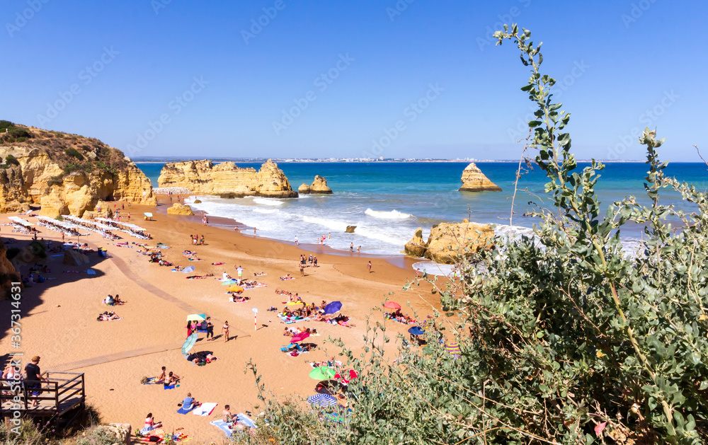 Tourists and locals enjoying famous Dona Ana beach with beautiful natural rock formations in Algarve, Southern Portugal. 