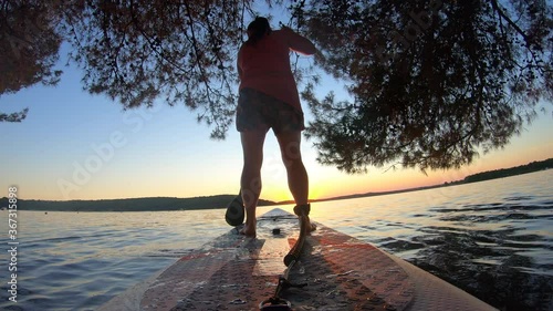 LD Low angle shot of a woman on a SUP paddling towards the sunset