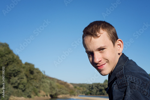 Portrait of a smiling young man by the river near the forest.