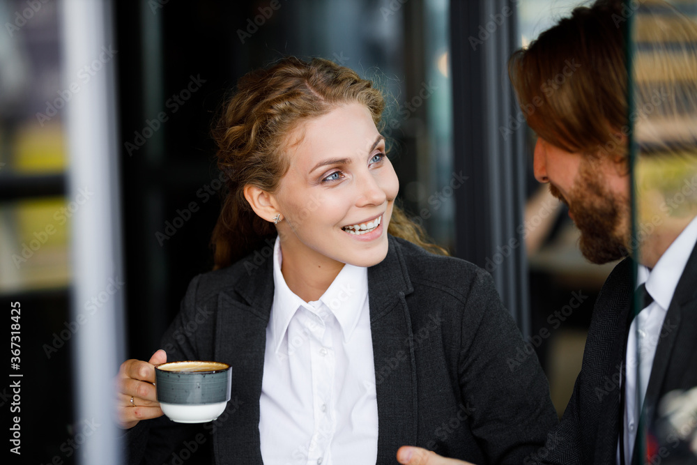 Charming and cute businesswoman with a smile communicates with a partner over a cup of coffee. Young european girl drinks coffee with a partner Charming and cute businesswoman with a smile communicates with a partner over a cup of coffee. Young european girl drinks coffee with a partner