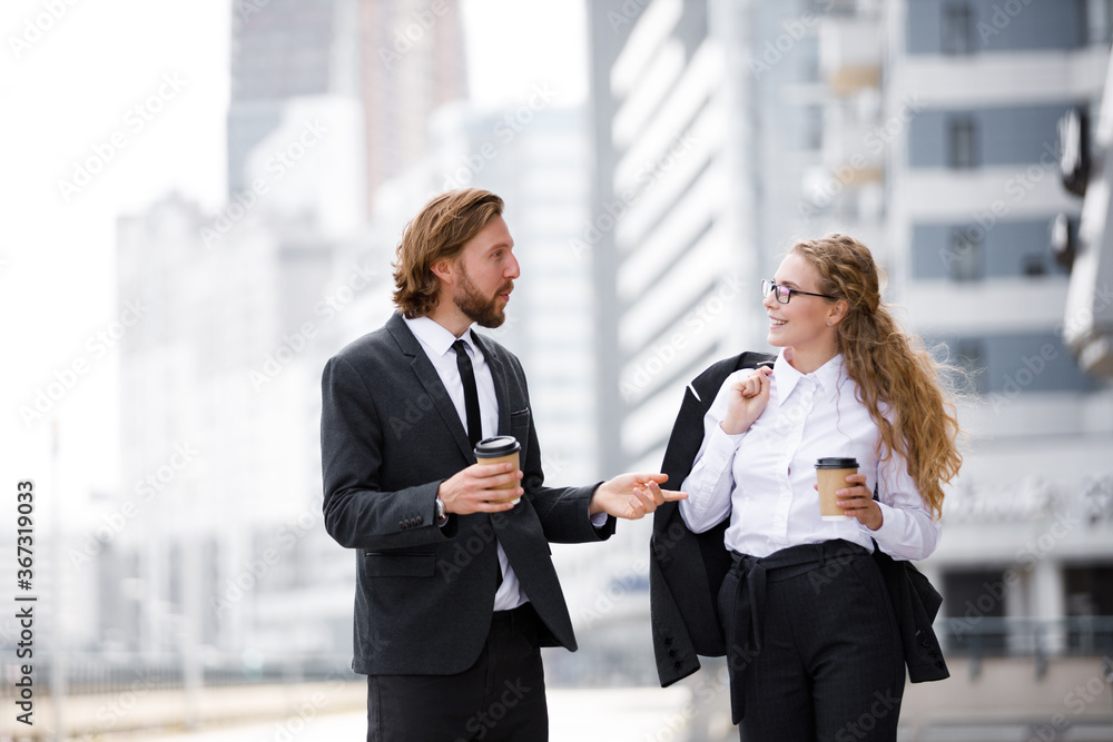 Young guy and a girl in a business suit are walking around the city with coffee and discussing plans Young guy and a girl in a business suit are walking around the city with coffee and discussing plans