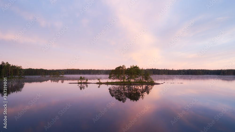 Beautiful calm lake with islands. Early misty summer morning with clouds. Pink sunset sky over wild lake. Cloud reflections in water.  Nature of Finland.
