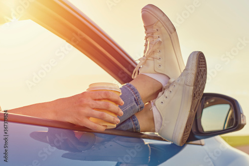 Roadtrip and freedom travel concept. Woman feet in sneakers on car window and cup of coffee in hand