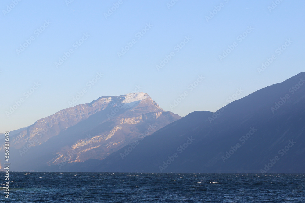 travel to snowy mountains in Italy, beautiful italian mountains neighboring lake Garda, lake along with mountains and blue sky, beautiful italian landscape with mountains