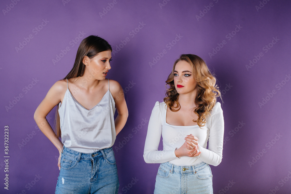 Two young and beautiful girls shows emotions and smiles in the Studio on a purple background. Girls for advertising Two young and beautiful girls shows emotions and smiles in the Studio on a purple background. Girls for advertising