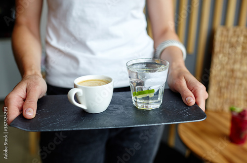 Female hands holding stone plate with cup of coffee and water in a glass with lime.Coffee break.Blurred image selective focus