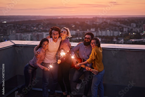 Happy friends with sparklers on rooftop in evening photo