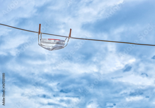 Washed white surgical face mask isolated hanging from a clothesline with a cloudy sky in the background. Misuse of face mask