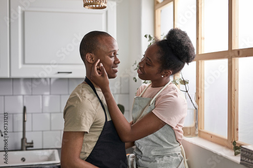 married black couple show their tender feelings while cooking in the kitchen. woman touch man's face and look at him with love
