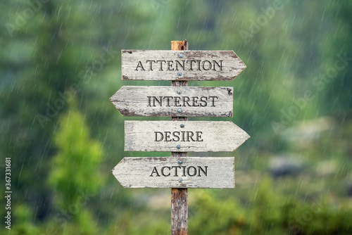 Attention interest desire and action text on wooden signpost outdoors in the rain.