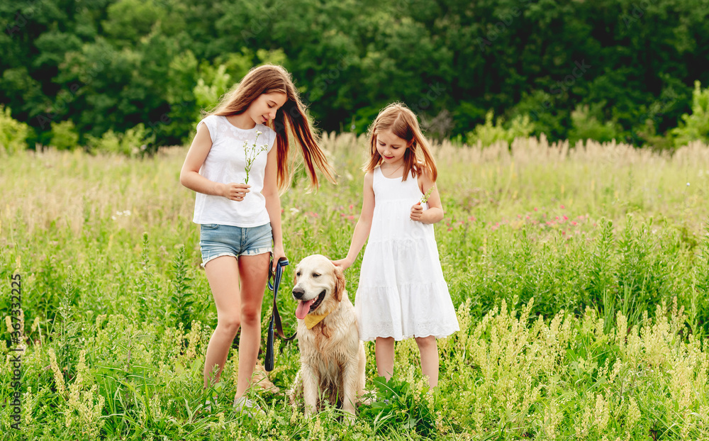 Sisters with dog on flowering meadow Sisters with dog on flowering meadow
