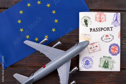 Flight to europe concept. European union flag with passport and toy airplane on dar wooden background.