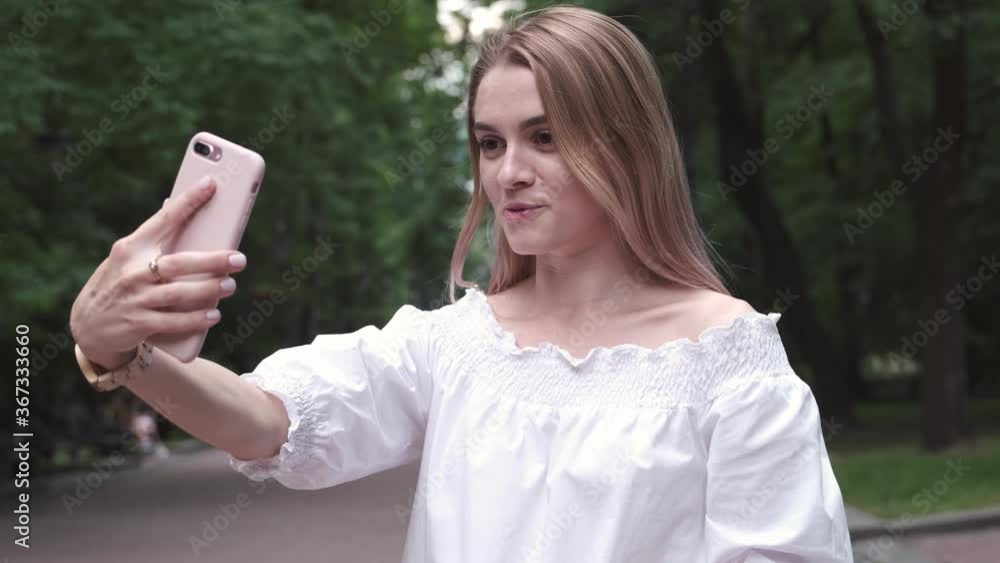 Beautiful Happy Young Girl Wearing White Dress Making a Video call Smiling Talking Relaxed on the Street City Background Close Up. Portrait of smiling woman having video call by mobile phone outdoors. Beautiful Happy Young Girl Wearing White Dress Making a Video call Smiling Talking Relaxed on the Street City Background Close Up. Portrait of smiling woman having video call by mobile phone outdoors.