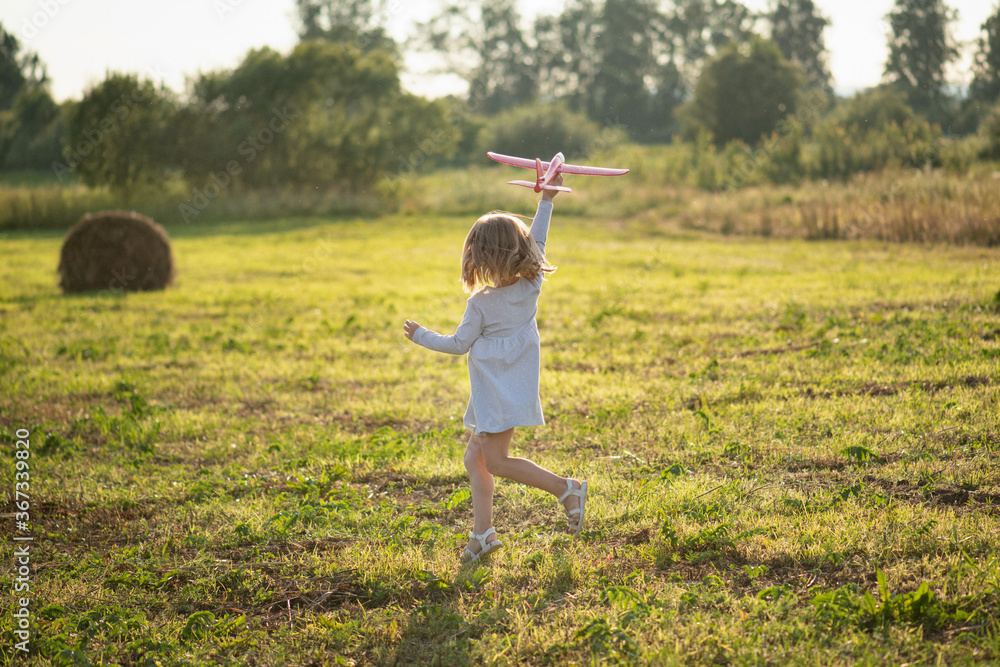 A girl in a dress runs across the field with a toy plane. The child imagines himself as a pilot. Dream of becoming an aviator A girl in a dress runs across the field with a toy plane. The child imagines himself as a pilot. Dream of becoming an aviator