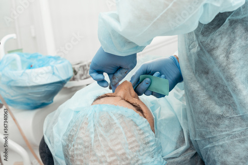 Patient and dentist during implant placement operation. Real operation. Tooth extraction, implants. Professional uniform and equipment of a dentist. Healthcare Equipping a doctor’s workplace. 